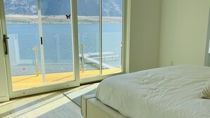 A bedroom with a large window overlooking a lake and mountains.
