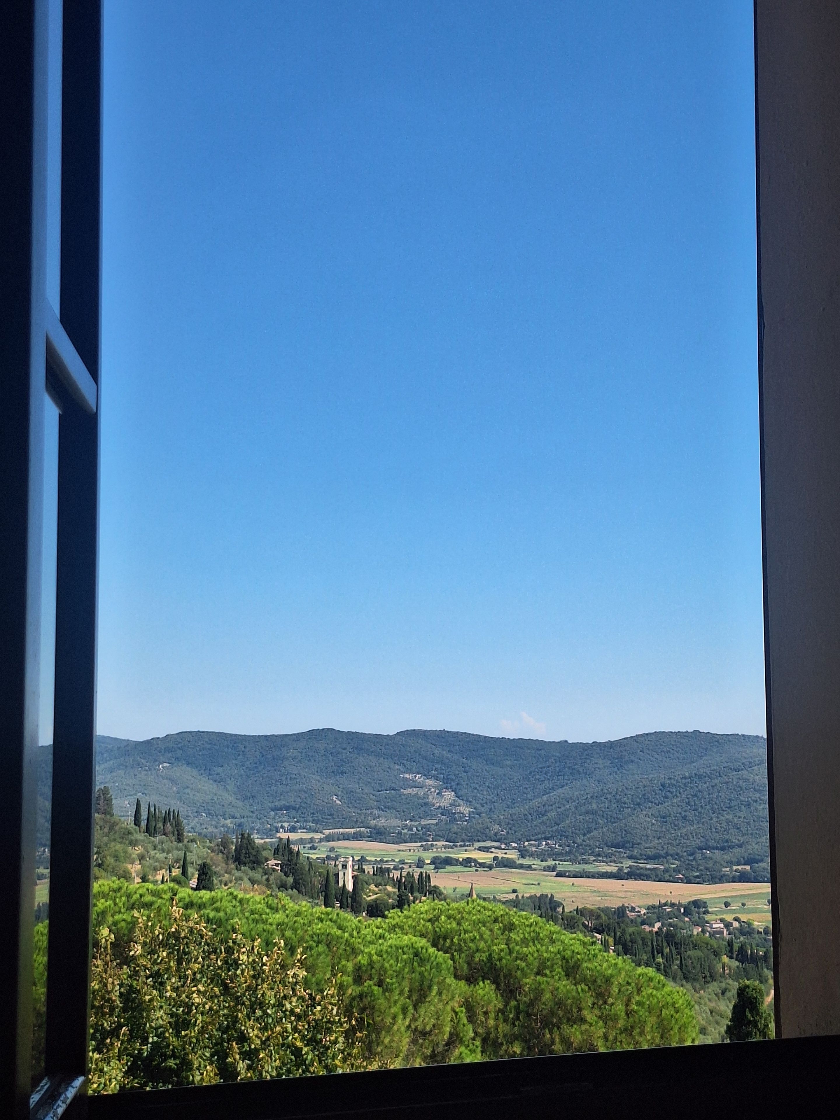 Une vue à travers une fenêtre sur un paysage composé de collines, d’arbres et d’un ciel dégagé.