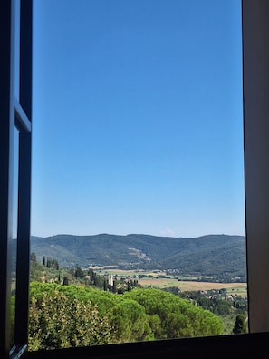Une vue à travers une fenêtre sur un paysage composé de collines, d’arbres et d’un ciel dégagé.