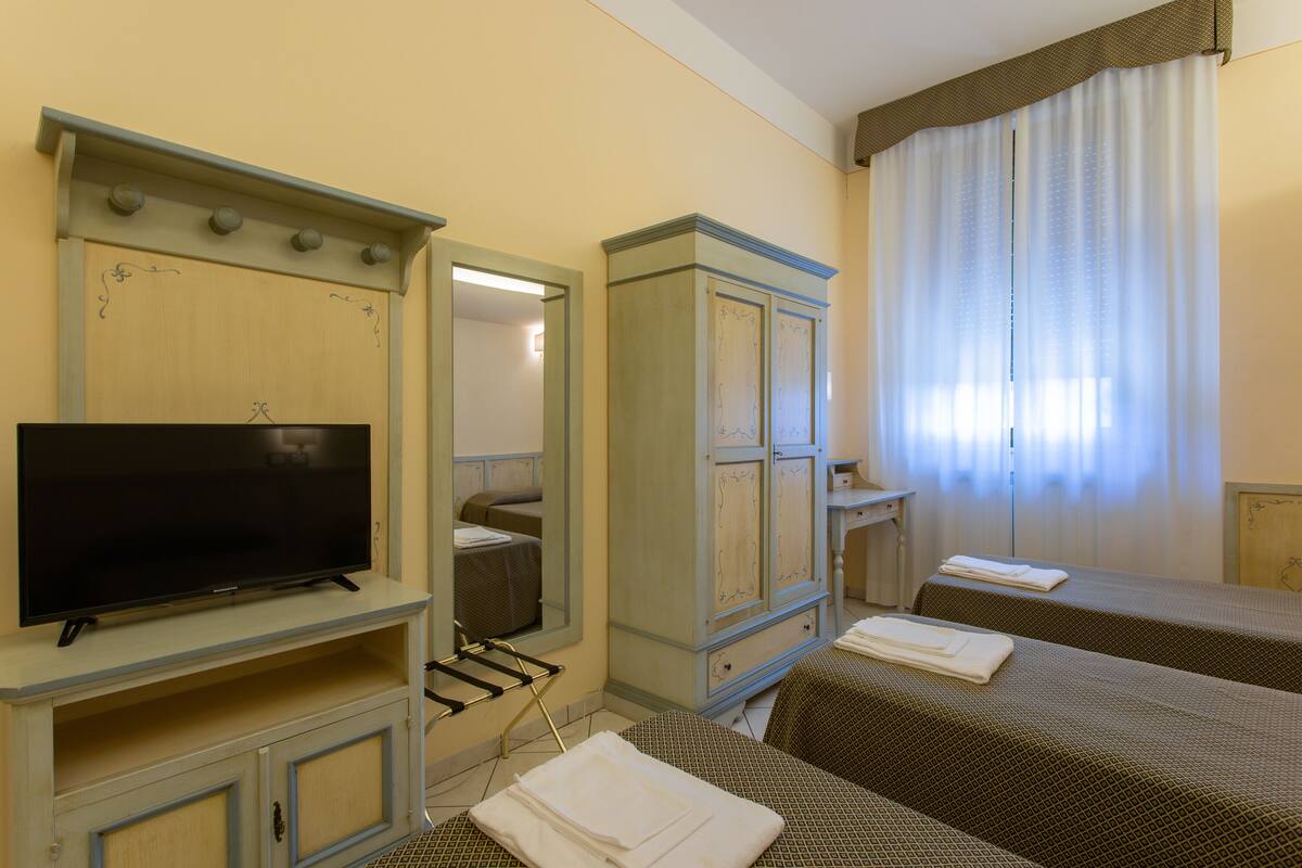 Ein Hotelzimmer mit Fernseher, Kleiderschrank, zwei Betten und einem Fenster mit Vorhängen.