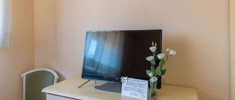 A television on a white desk with a vase of white flowers and a sign.