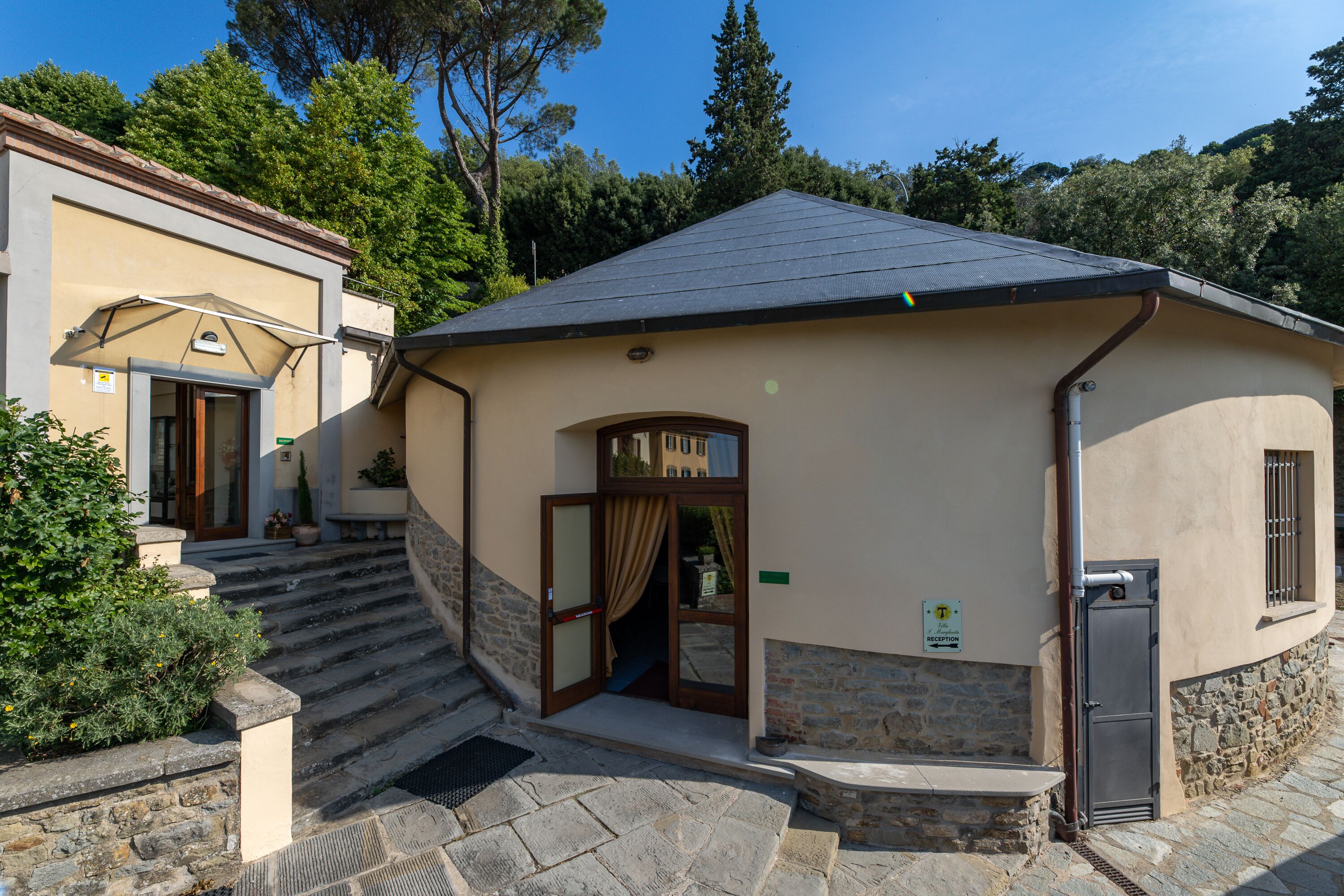 A building with a stone staircase leading to a door with a curtain, a reception sign, and a small window with bars.