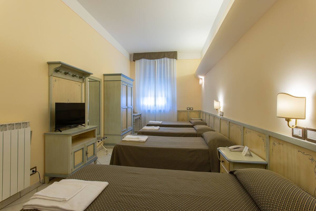 Ein Hotelzimmer mit drei Betten, einem Fernseher, einem Spiegel und einem Nachttisch mit Lampe.