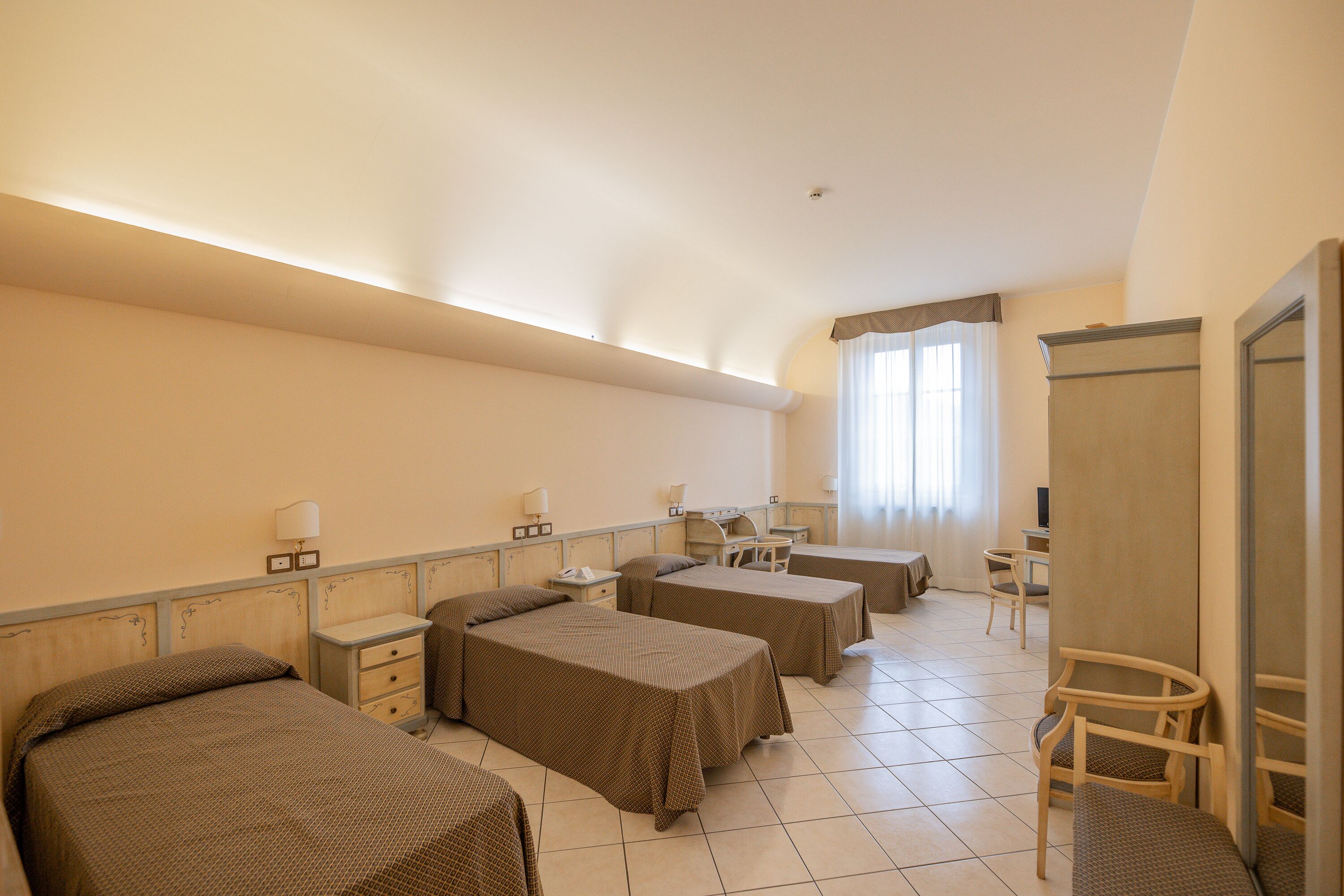 A hotel room with three beds, a desk, a chair, and a wardrobe.