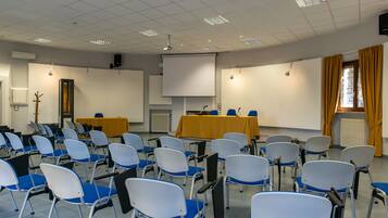 Une salle de conférence avec des rangées de chaises, un écran de projection et une table recouverte d’une nappe jaune.