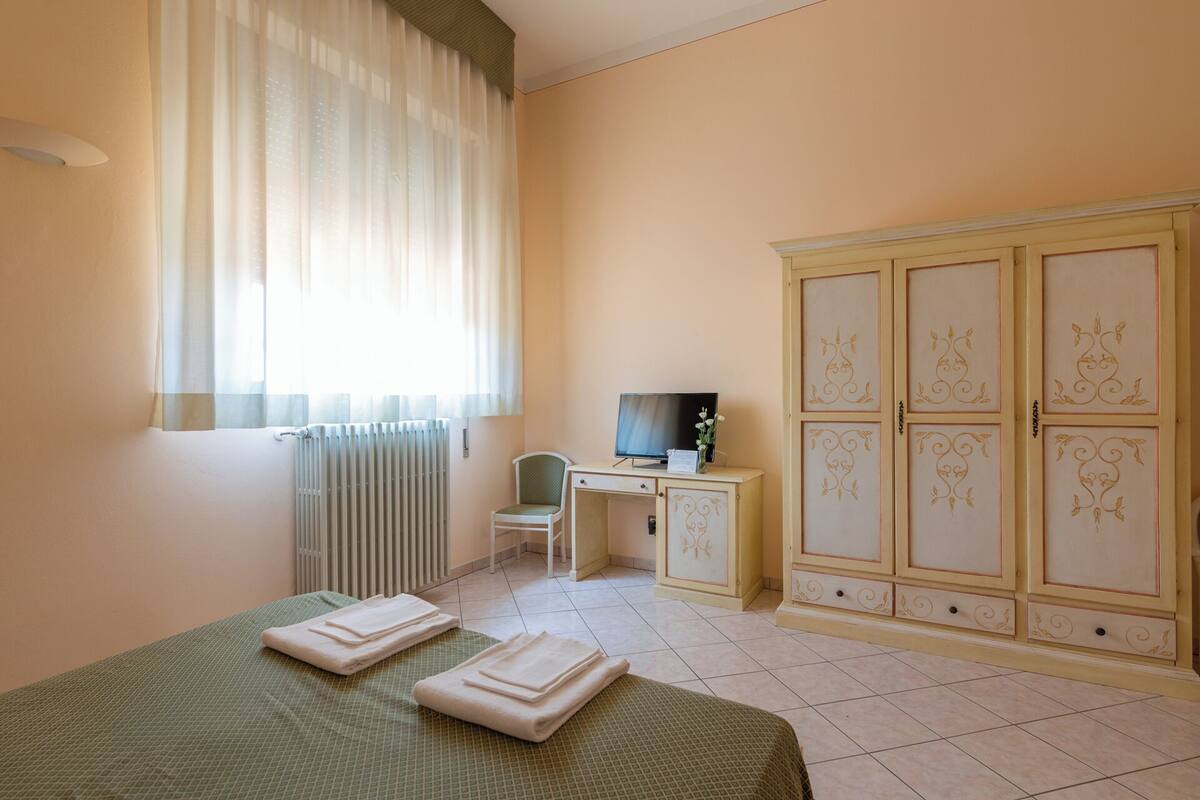 Ein Schlafzimmer mit Bett, Schreibtisch, Stuhl, Heizkörper und Kleiderschrank.