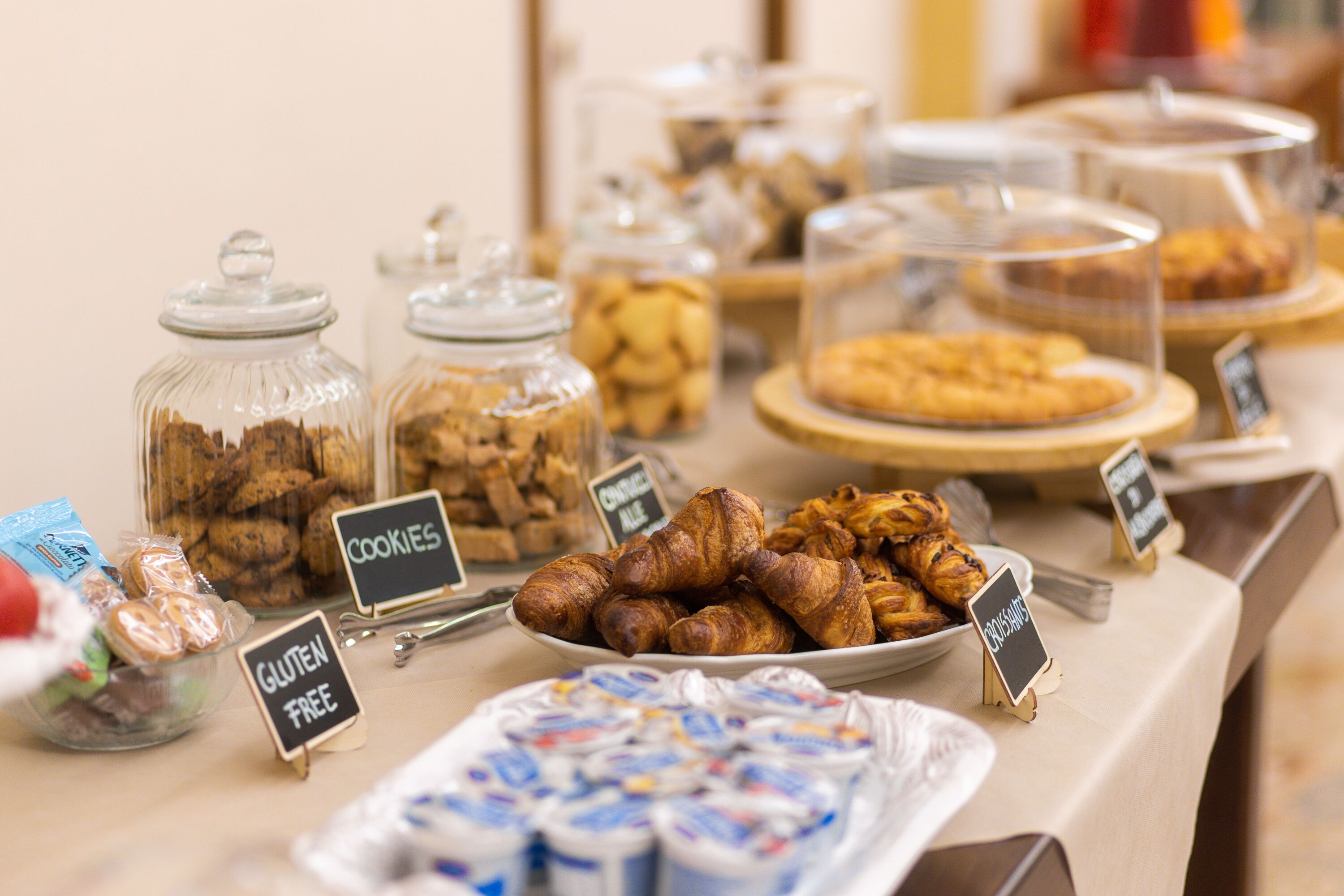 A buffet with labeled sections for cookies, gluten-free options, and croissants.
