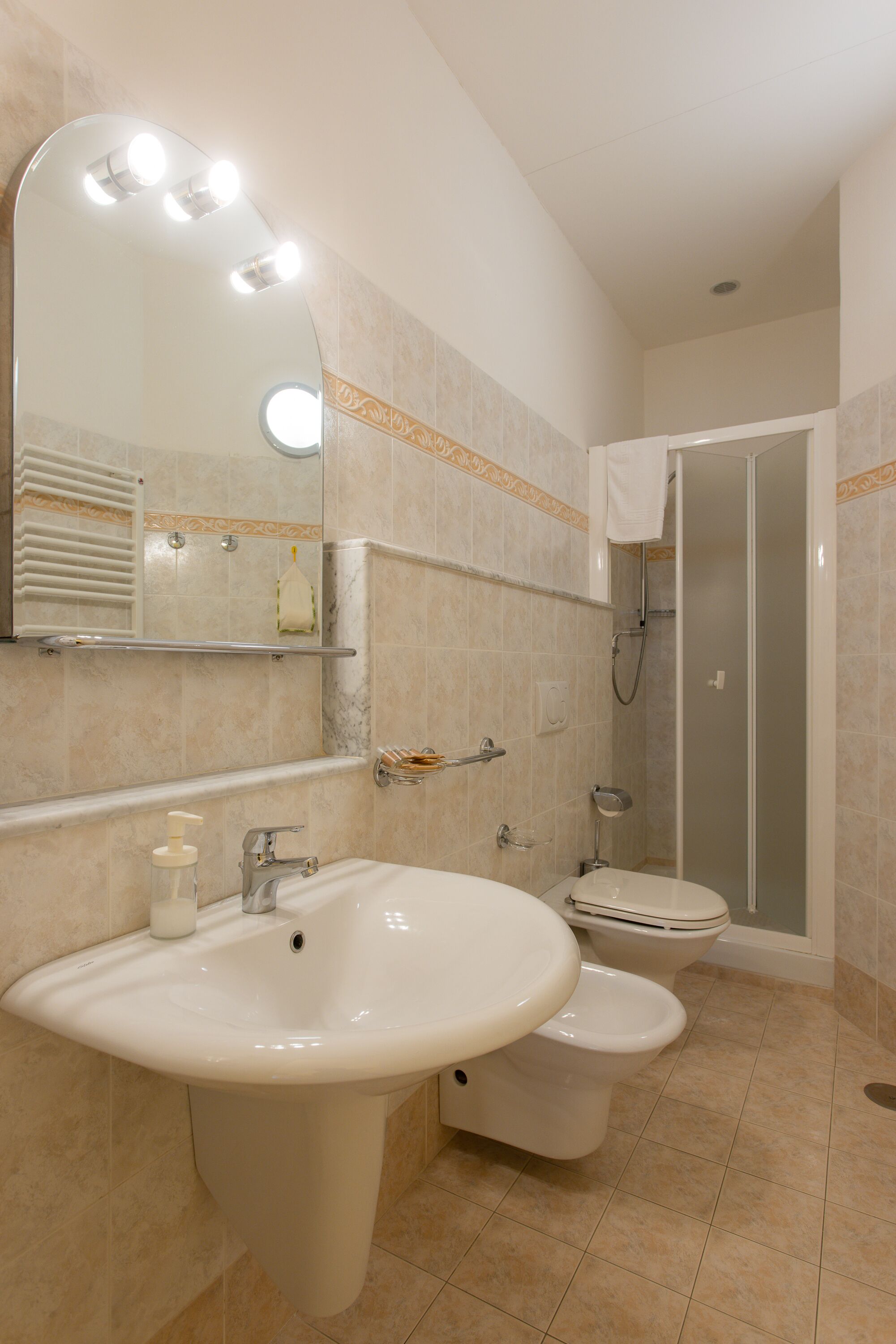 A bathroom with a large sink, a toilet, a shower, and a mirror with lights.