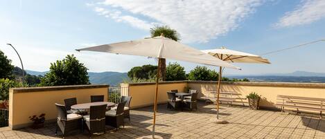 A rooftop terrace with outdoor furniture, a large umbrella, and a view of the landscape.