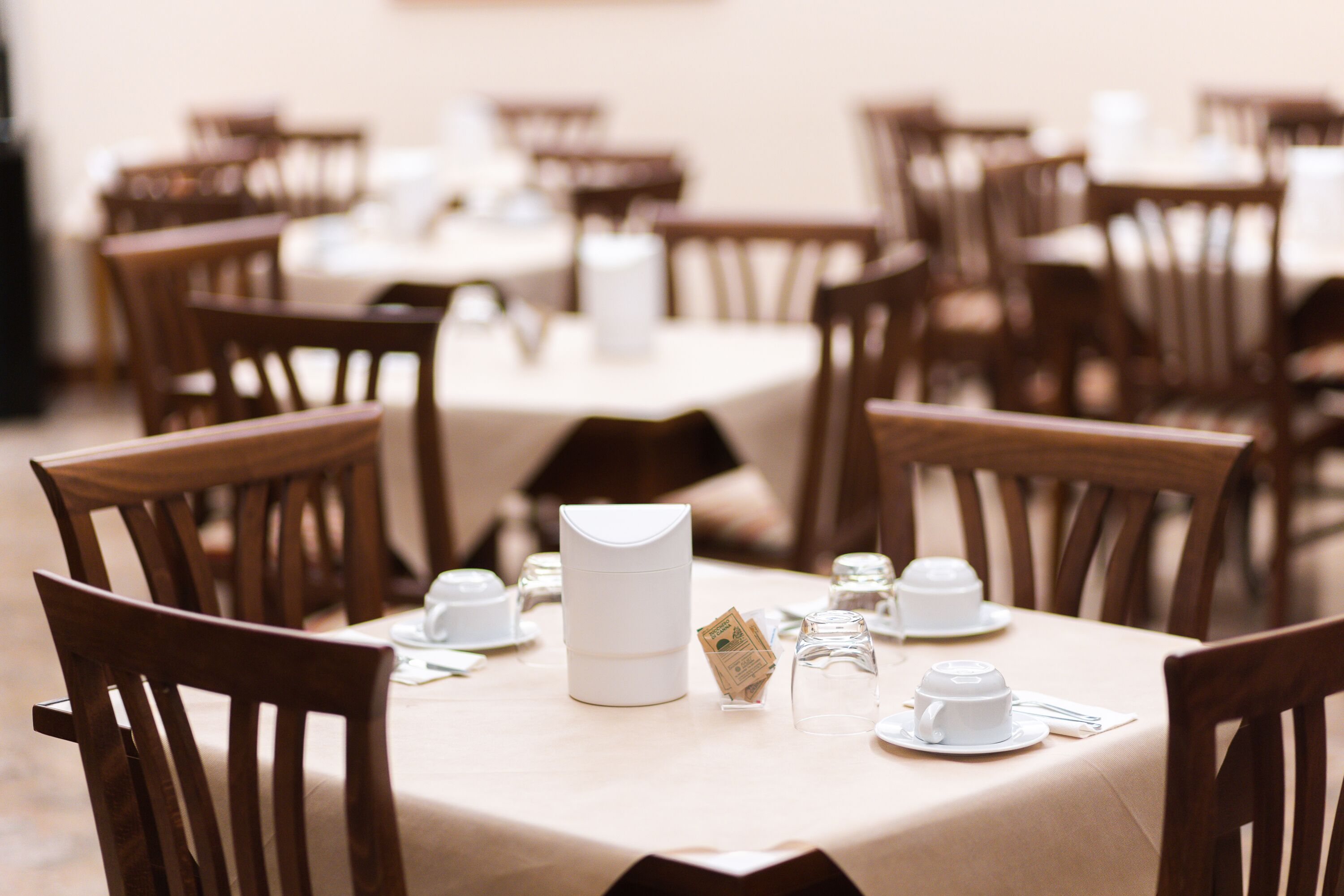 Comedor con mesas dispuestas para el servicio, con manteles blancos y sillas de madera.