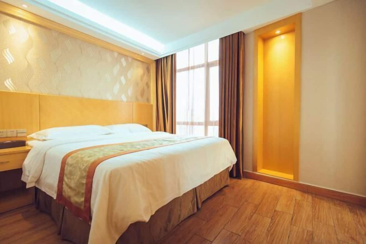 Habitación de hotel con cama doble, cabecera de madera, mesita de noche y un gran ventanal con cortinas.