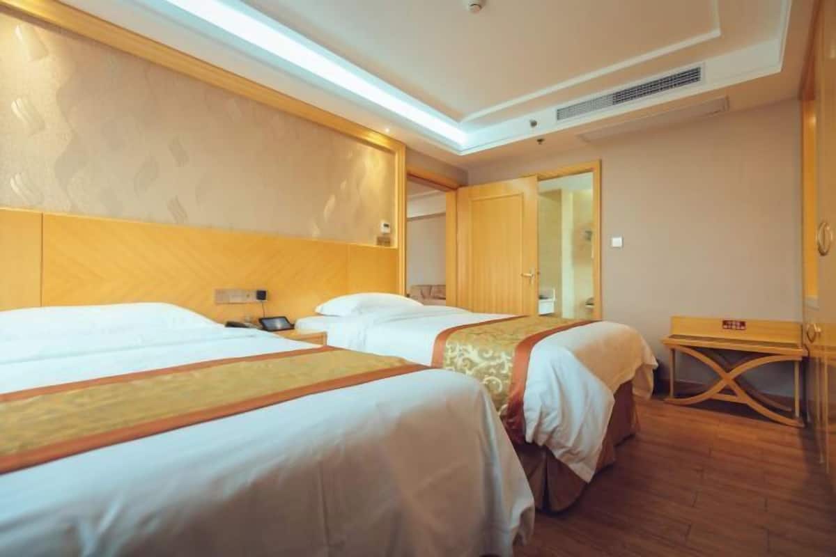 Habitación de hotel con dos camas, cabecero de madera, mesita de noche y espejo.