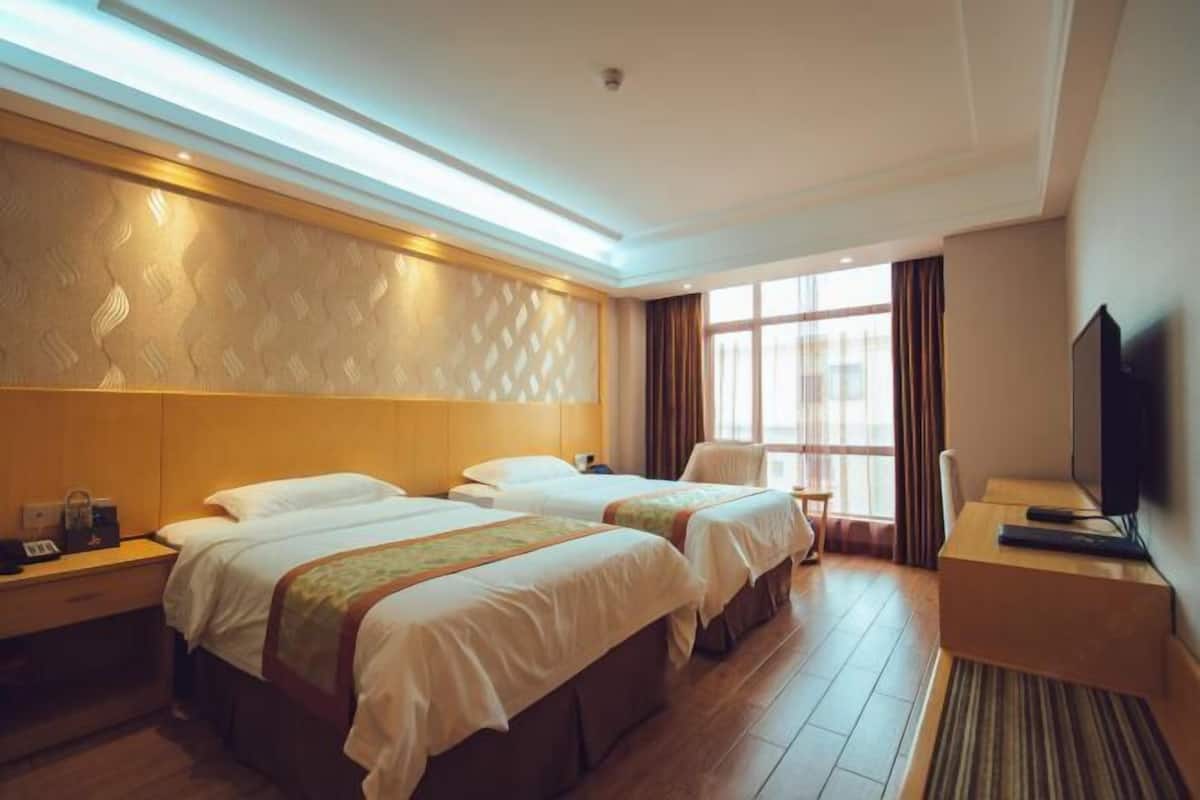 Habitación de hotel con dos camas, televisión, escritorio y ventana con cortinas.