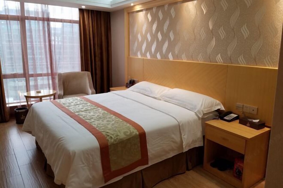 A hotel room with a large bed, a bedside table, a chair, and a small table.