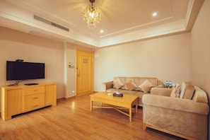 A living room with a wooden floor, a television on a cabinet, a sofa, and a coffee table. - Jing Hao Hotel (Shanwei)