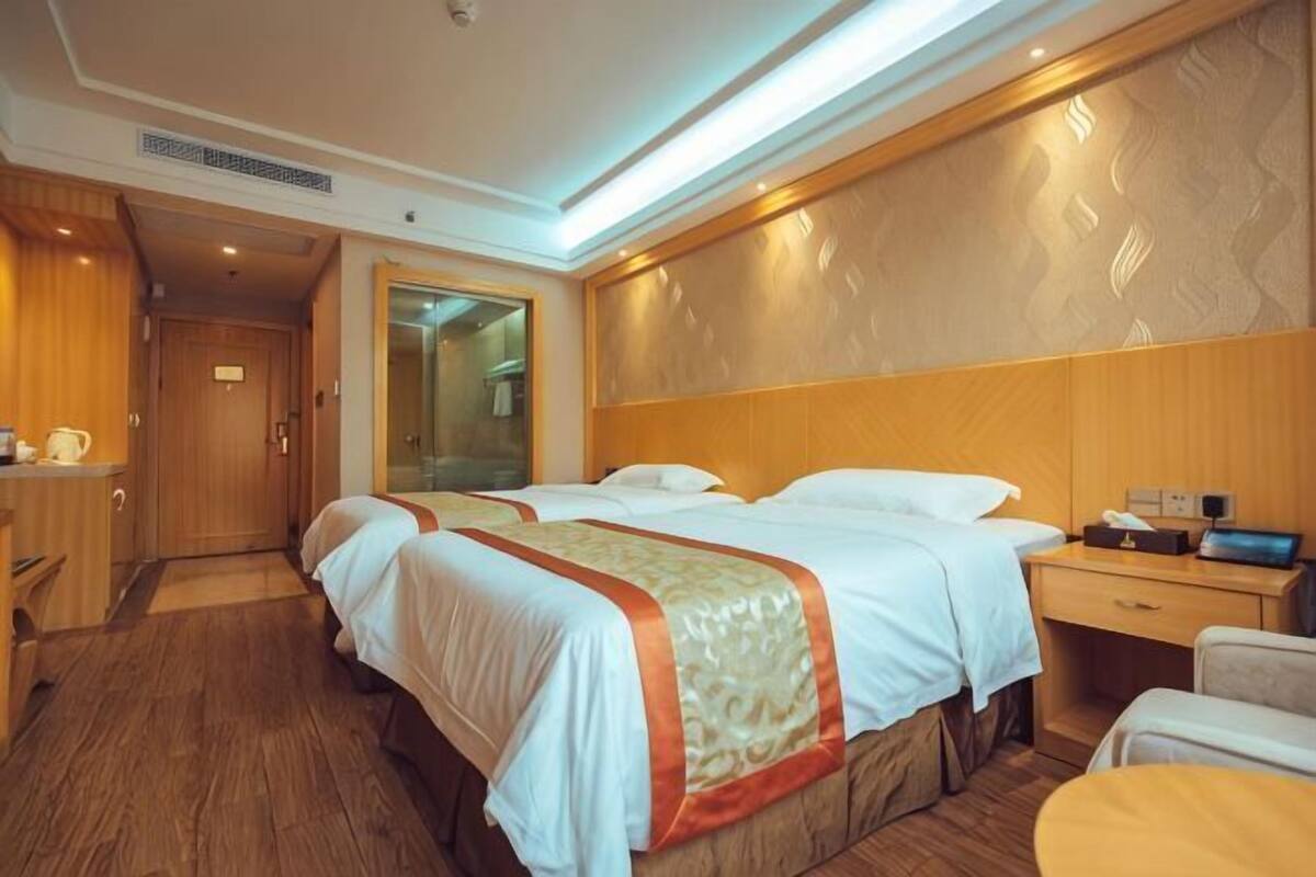 Habitación de hotel con dos camas, cabecero de madera, escritorio con silla y una mesita.