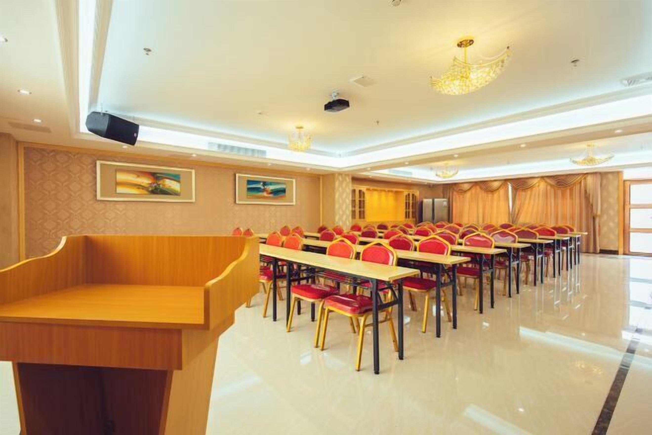 A conference room with rows of tables and chairs, a podium, and a chandelier.
