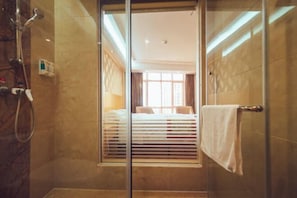 A hotel room with a glass shower enclosure, a bed with a white headboard, and a towel rack. - Jing Hao Hotel (Shanwei)