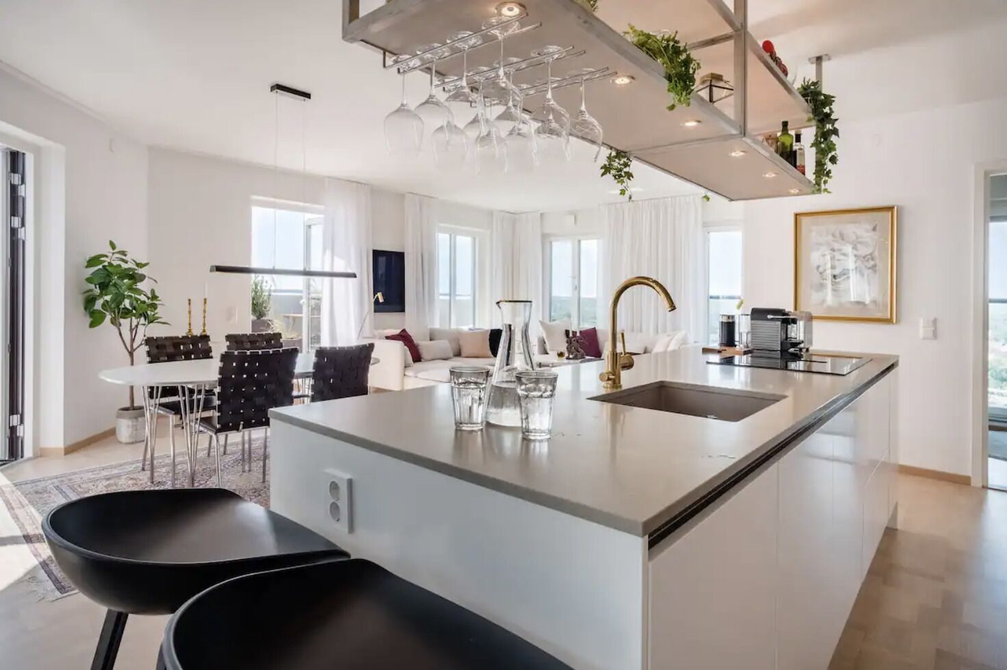 Une cuisine moderne dotée d’un îlot central, un coin repas avec une table blanche et des chaises noires, et un salon avec un canapé et une table basse.