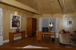 A room with a wooden ceiling, a desk with a lamp, a chair, and a framed picture on the wall. - Yingxue Hotel (Dayi)