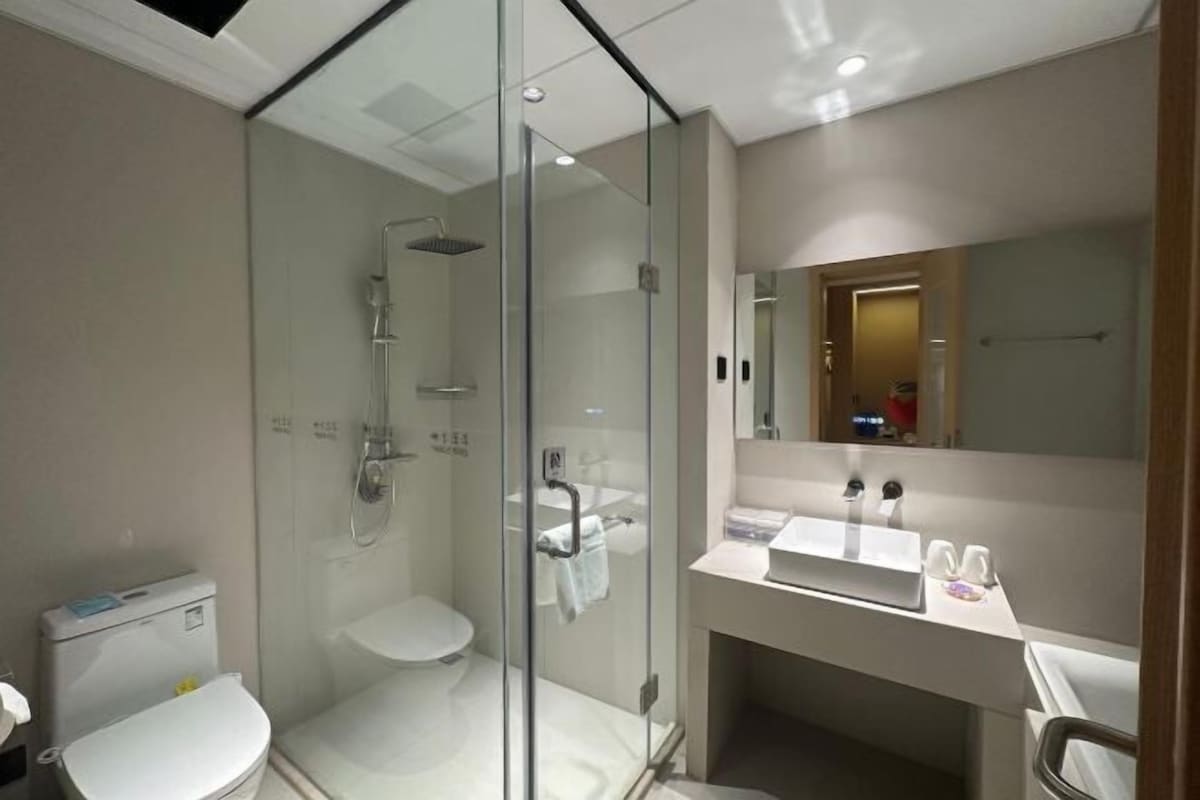 A modern bathroom with a glass-enclosed shower, a toilet, and a sink with a mirror above.