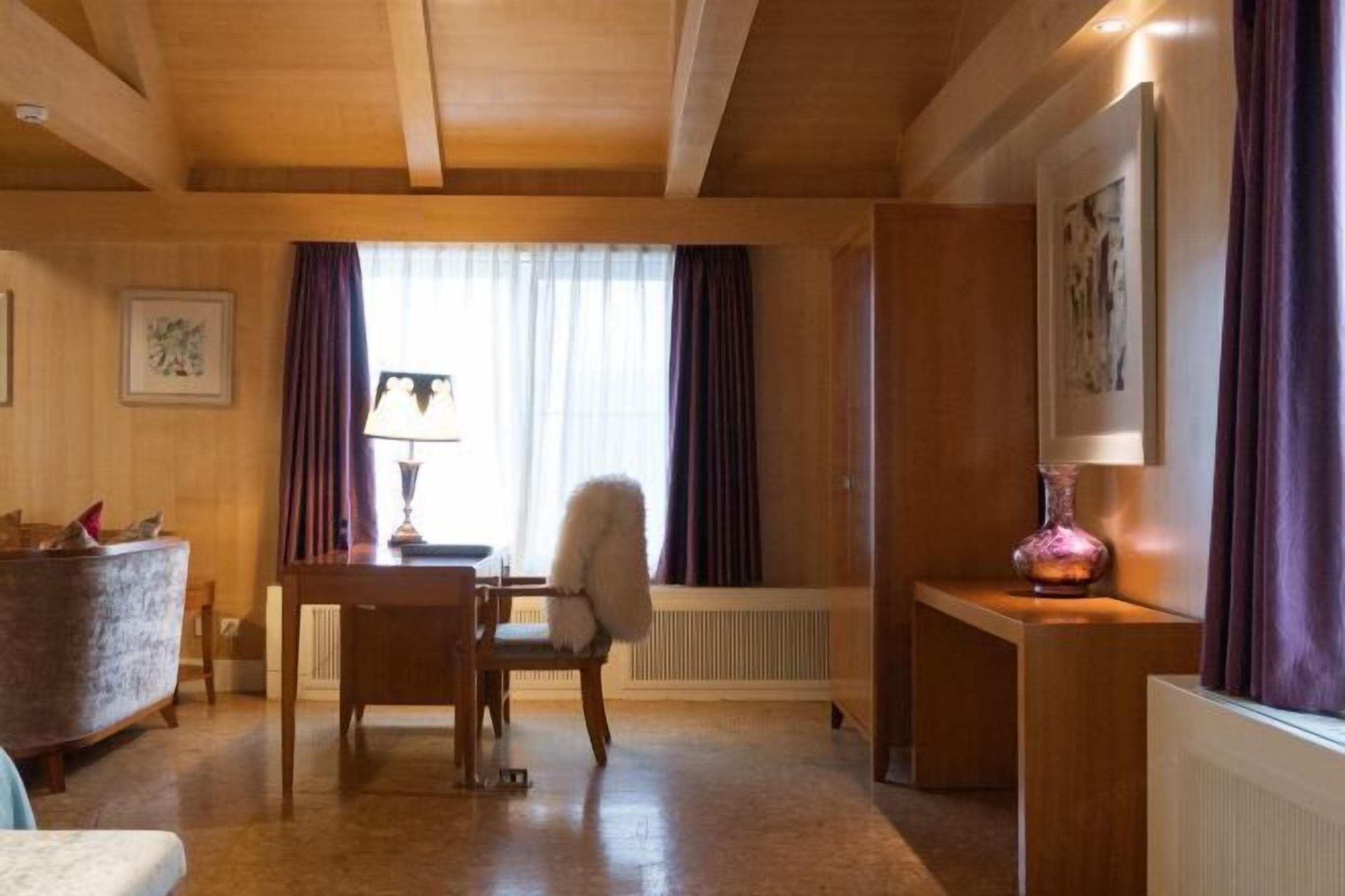 A room with wooden ceiling beams, a dining table with chairs, a radiator, and a lamp on a side table.