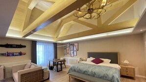Une chambre d’hôtel moderne dotée d’un grand lit, d’un coin salon avec un canapé et un fauteuil, d’une petite table et d’un lustre.
