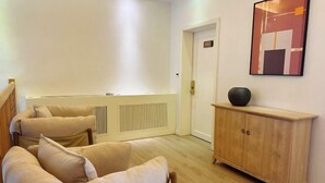 Une pièce comprenant un canapé de couleur beige, un meuble en bois et un tableau abstrait encadré accroché au mur.