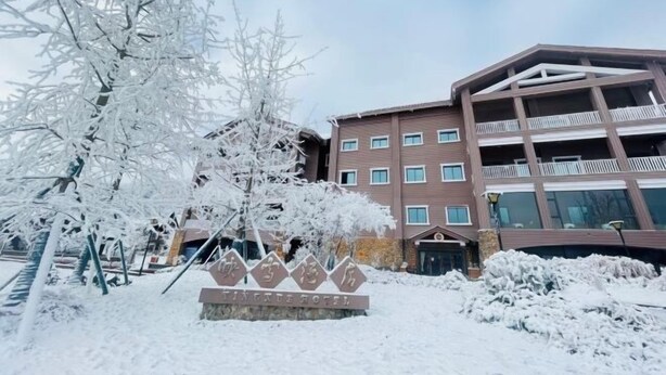 Un bâtiment d’hôtel à plusieurs étages, doté de balcons, entouré d’arbres couverts de neige et sur lequel on peut voir une enseigne indiquant le nom de l’hôtel.