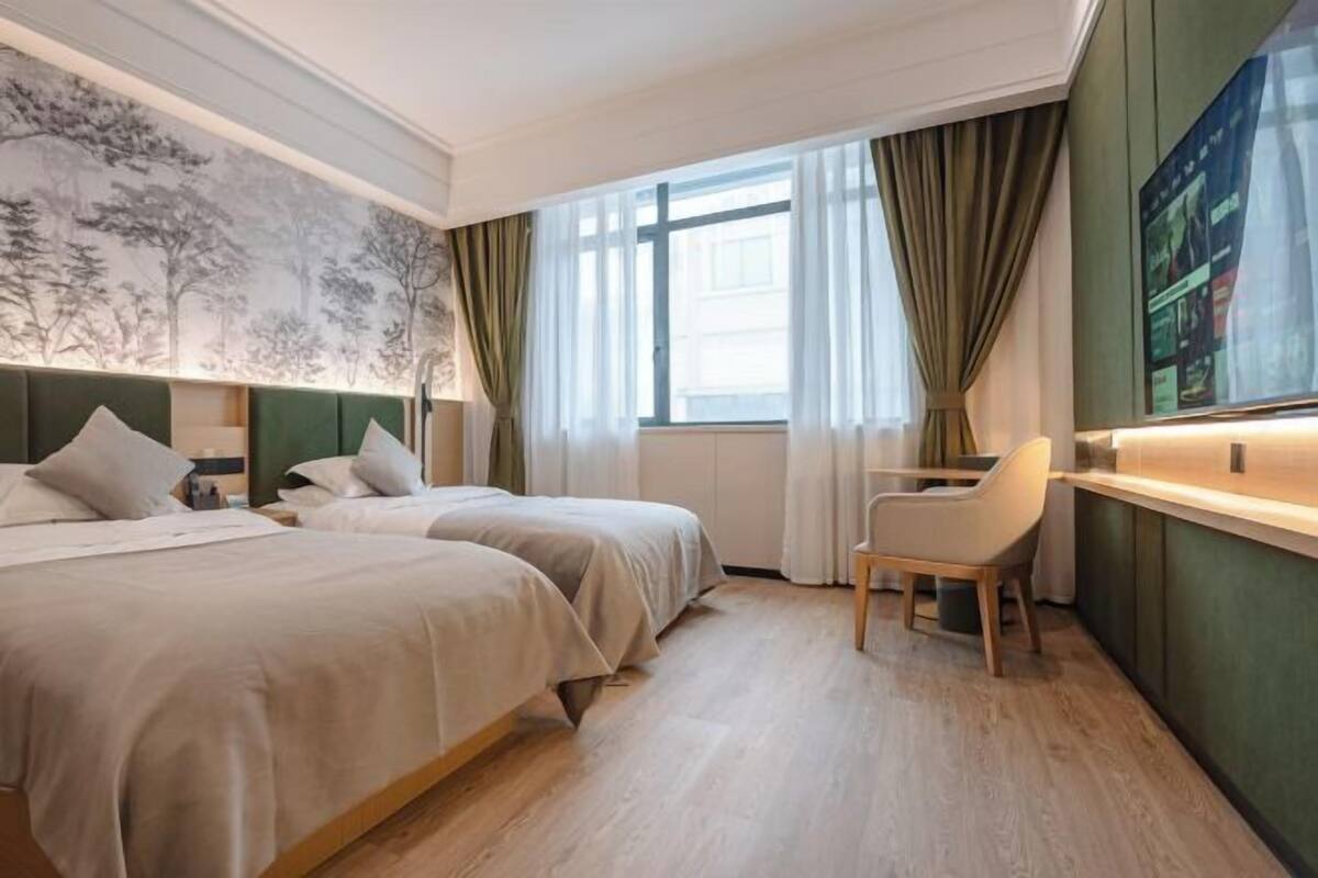 A hotel room with two beds, a desk, a chair, and a large window with curtains.