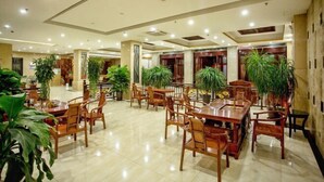 A spacious hotel lobby with multiple wooden tables and chairs, surrounded by potted plants. - Ledong Fuhua Haoting Hotel (Huangliu Branch) (Ledong)