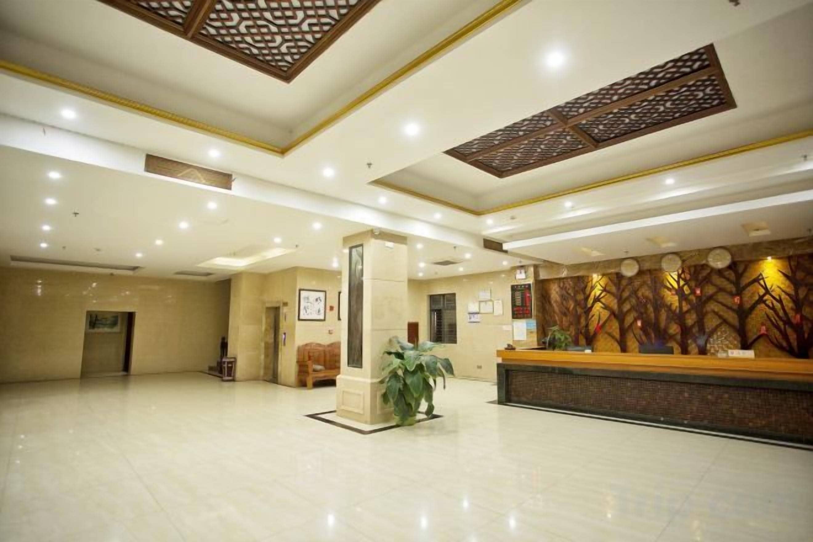 A hotel lobby with a reception desk, a large plant, and a decorative wall.