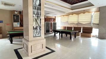 Un vaste espace intérieur comprenant une table de billard, une table de snooker et une grande colonne ornée d’un motif décoratif.