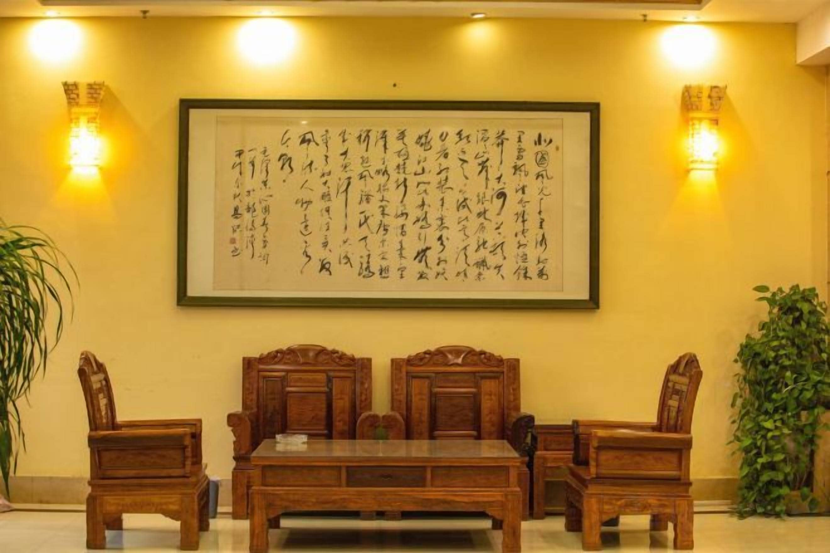 A traditional room with a wooden table and chairs, a framed calligraphy artwork on the wall, and two wall-mounted light fixtures.