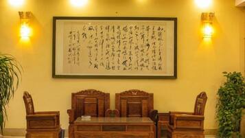 A traditional room with a wooden table and chairs, a framed calligraphy artwork on the wall, and two wall-mounted light fixtures.