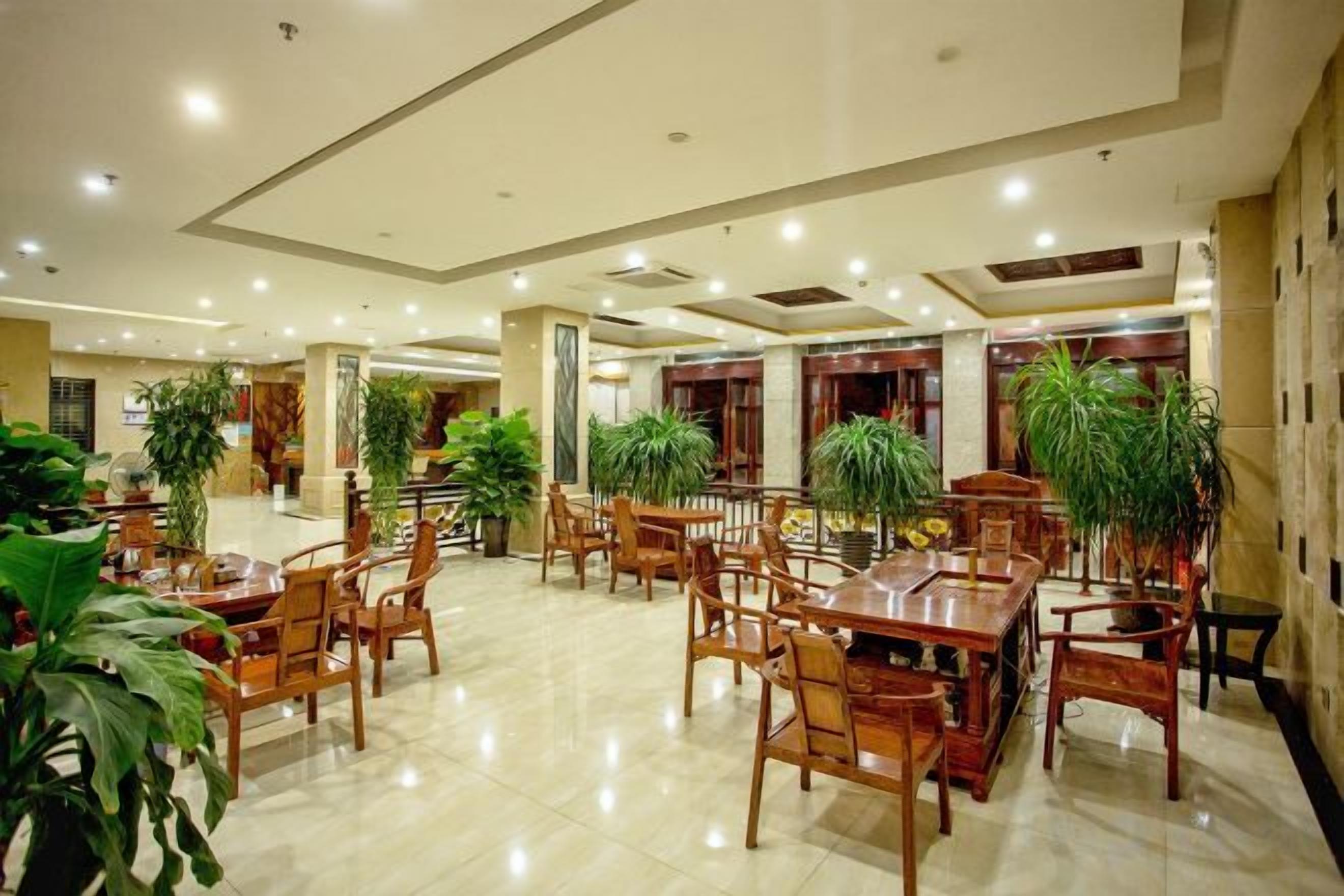 A spacious indoor dining area with multiple wooden tables and chairs, surrounded by potted plants.