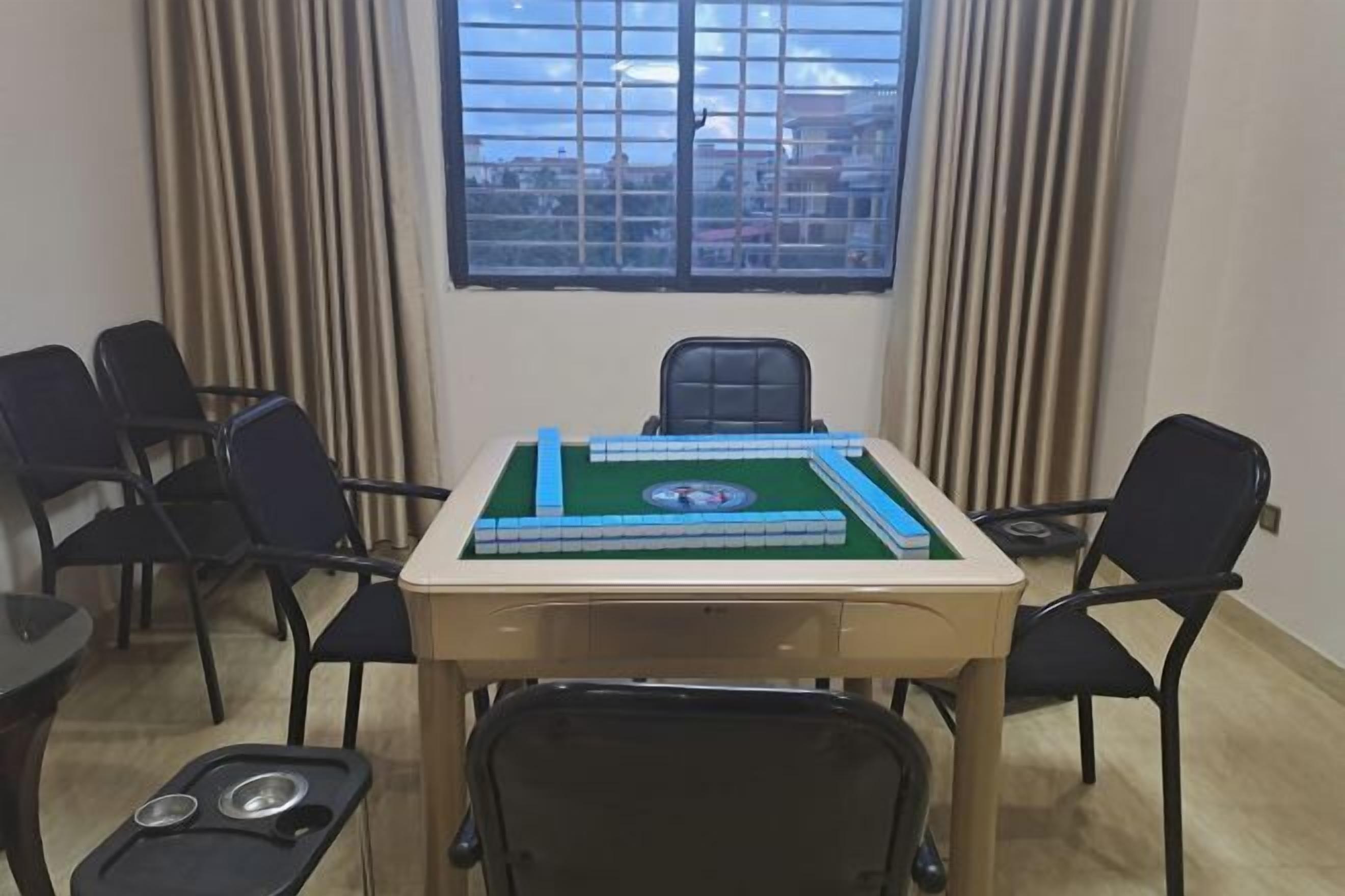 Una habitación con una mesa dispuesta para dos personas, una ventana con persianas y vistas a edificios.