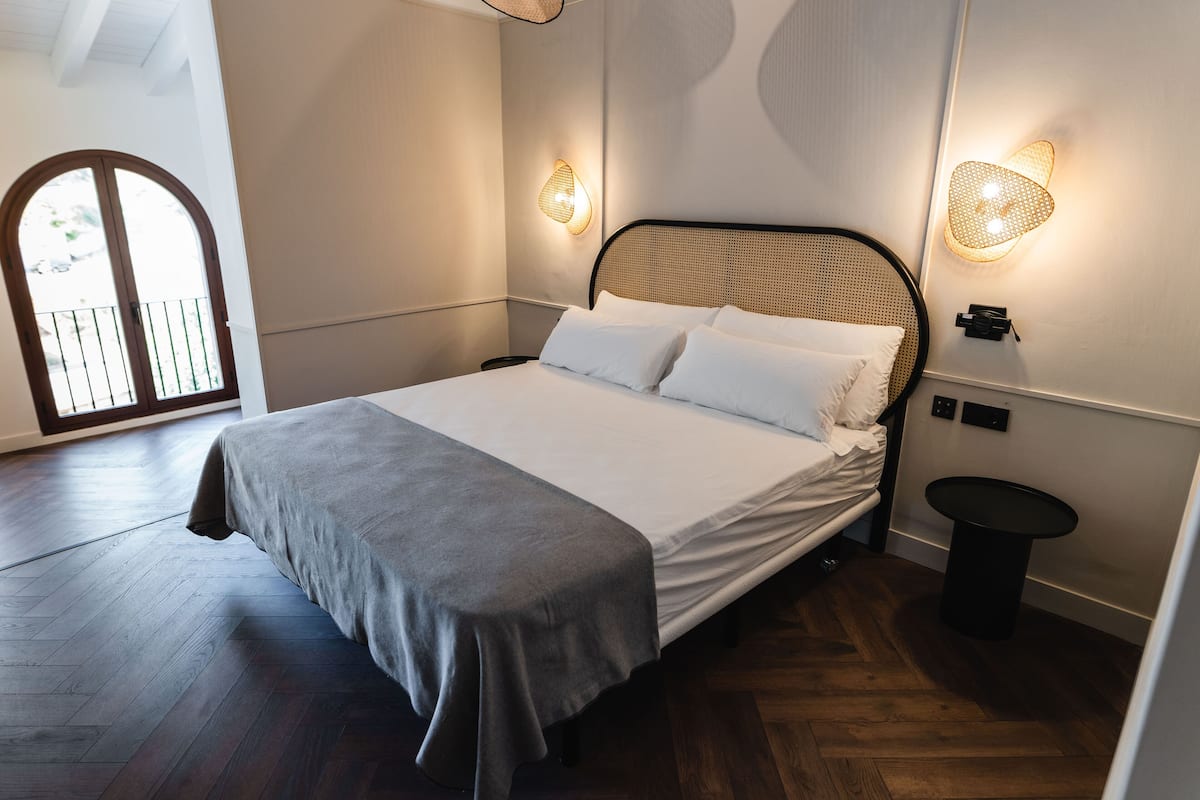A neatly made bed with a grey bedspread and white pillows in a room with wooden flooring.