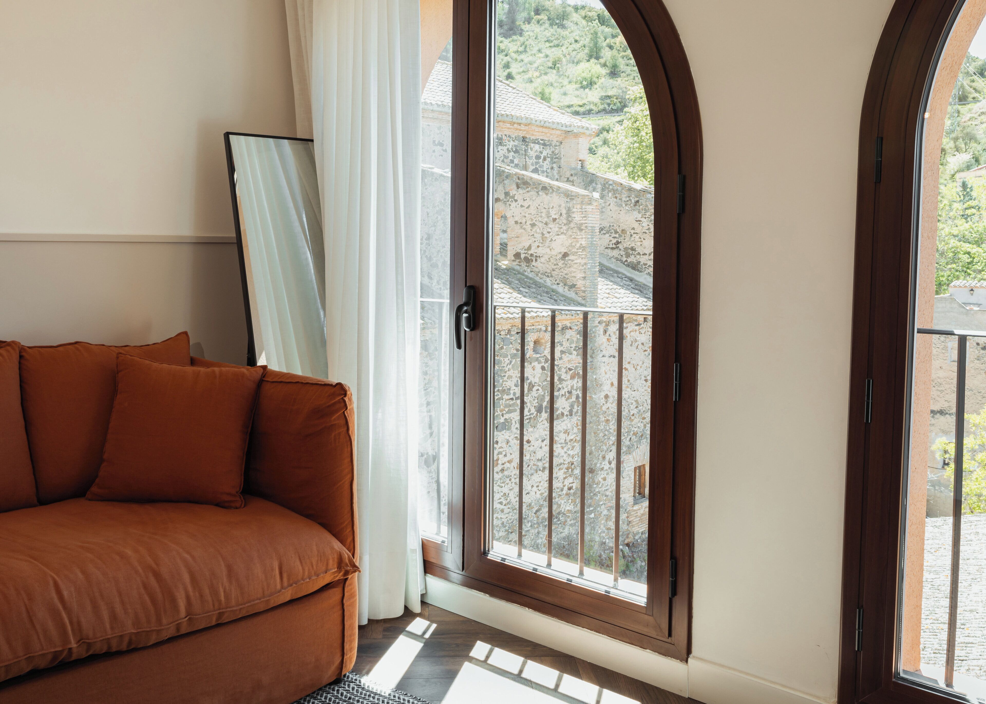 Una habitación con un sofá marrón, un ventanal con vistas a edificios y una puerta con un panel de vidrio.