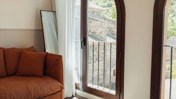 Una habitación con un sofá marrón, un ventanal con vistas a edificios y una puerta con un panel de vidrio.