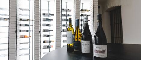 A table with three wine bottles in a room with large windows and a brick wall.