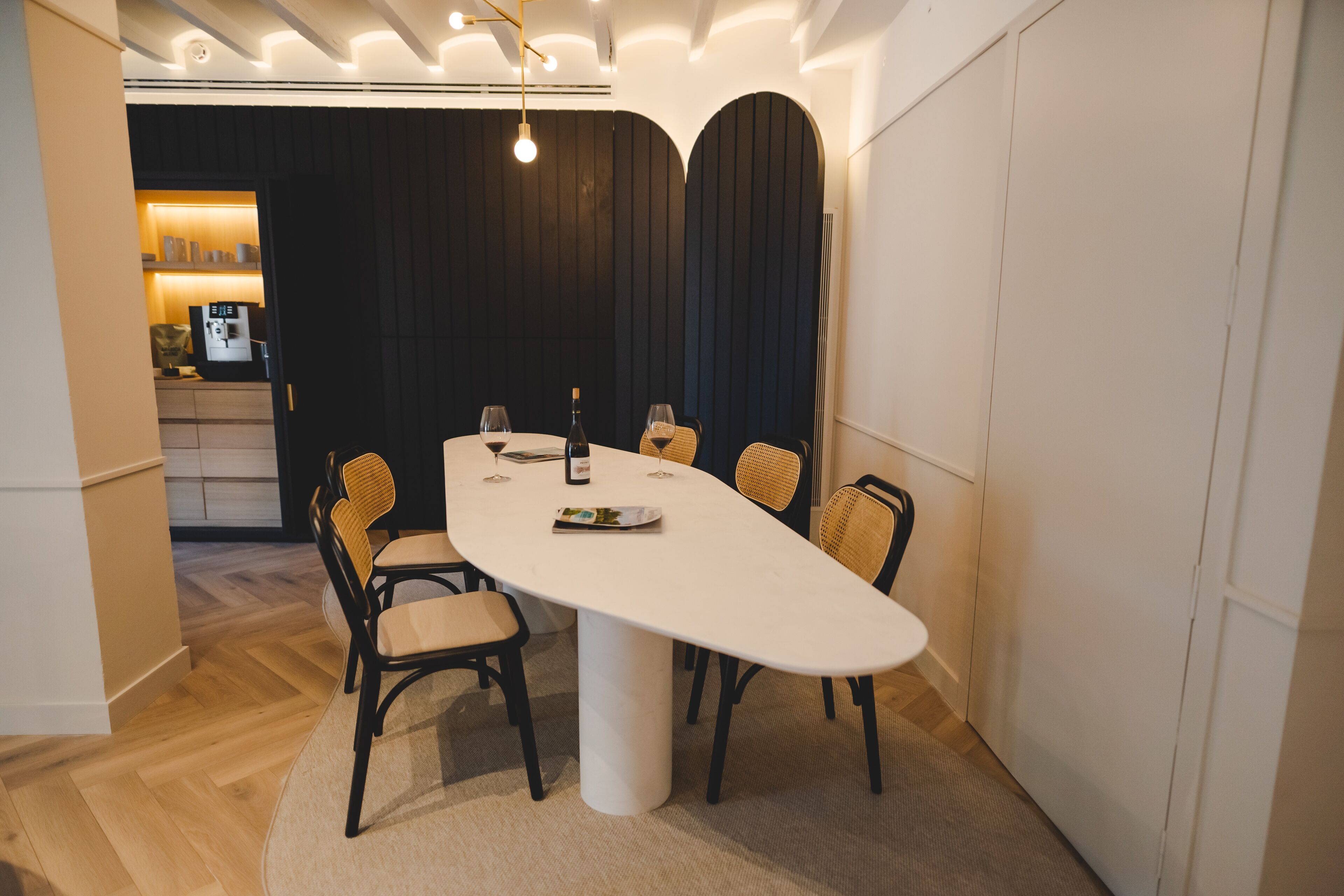 A modern dining area with a white table, six chairs, and a bottle of wine.