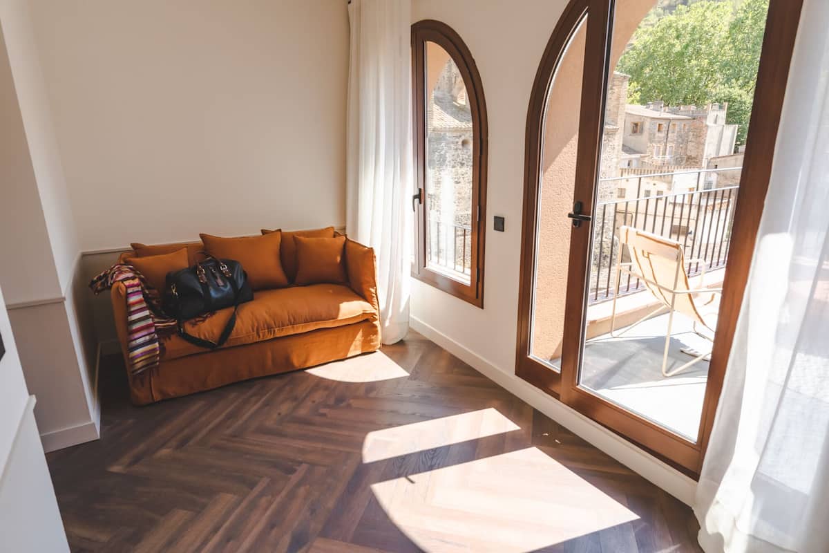 A corner room with a brown sofa, a black bag, and a window with a view of buildings and trees.