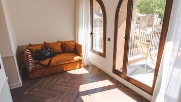 A corner room with a brown sofa, a black bag, and a window with a view of buildings and trees.