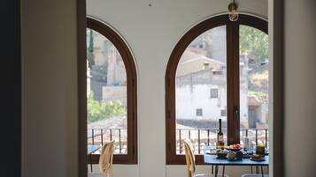 Un comedor con dos ventanas arqueadas, una mesa dispuesta con platos, una botella y sillas.