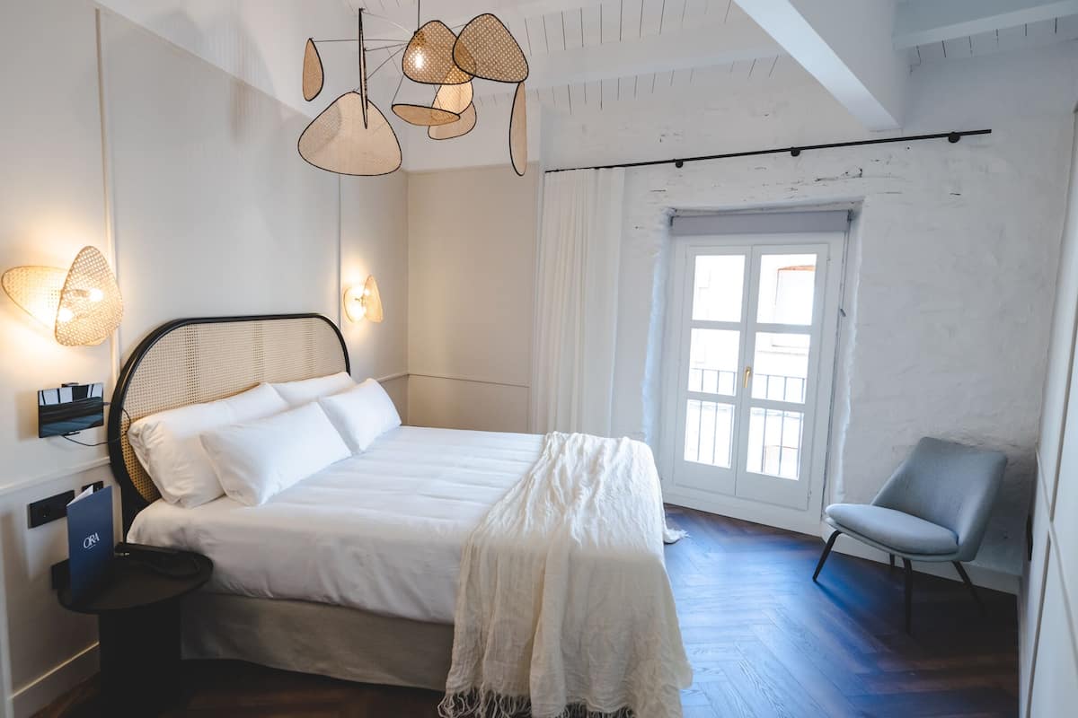 A bedroom with a bed, bedside table, chair, and a window with curtains.