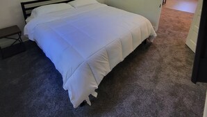 A bedroom with a bed, a nightstand, a painting of a dog, and a door leading to another room. - The Lakeside Micro Apartment (Muskegon)