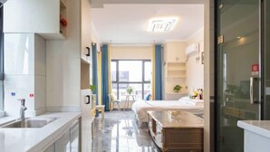 A modern hotel room with a kitchen area, a bed, and a view of the city. - Huaxi Guesthouse (Zhangjiajie)