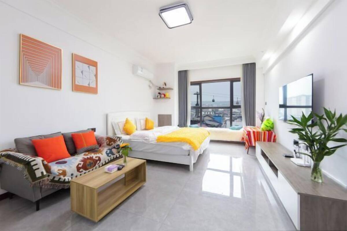 A modern hotel room with a bed, sofa, and a small table. There is a balcony with a view of the city.