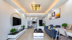 A modern living room with a flat-screen TV, a coffee table, a sofa, and a dining area with a table and chairs. - Huaxi Guesthouse (Zhangjiajie)